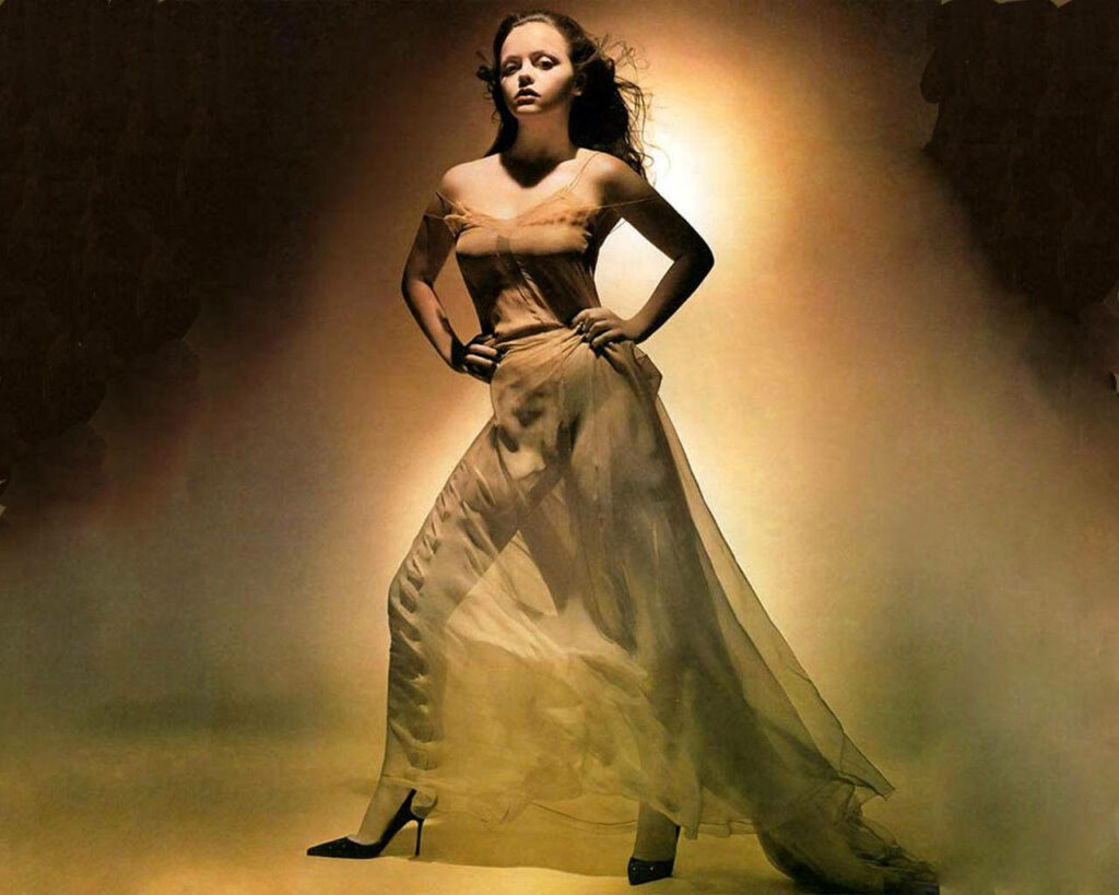 Christina Ricci in elegant sheer outfit with warm dramatic lighting showcasing her grace and style Wallpaper