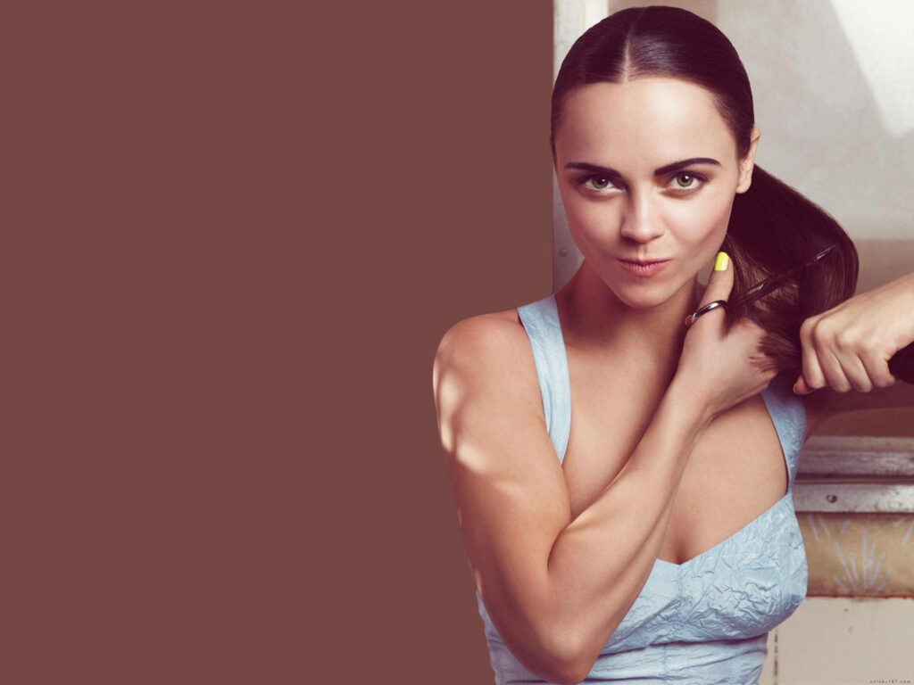 Christina Ricci playfully pretending to cut her long hair with a confident mischievous smile Wallpaper