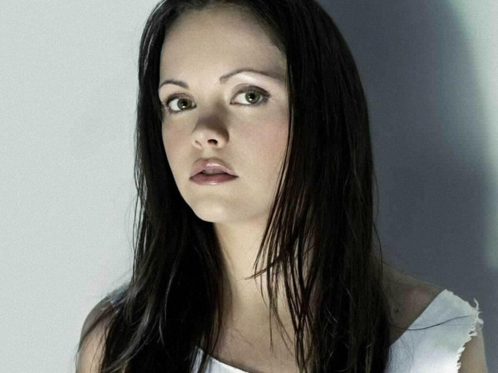 Christina Ricci in white top with dark hair and expressive gaze on soft neutral wallpaper background