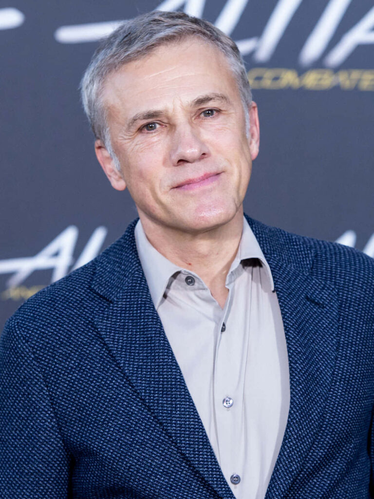 Christoph Waltz in blue blazer portrait with dark blurred background and event text wallpaper