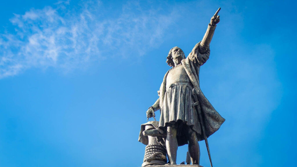 Statue of Christopher Columbus pointing forward against vivid blue sky for Columbus Day wallpaper