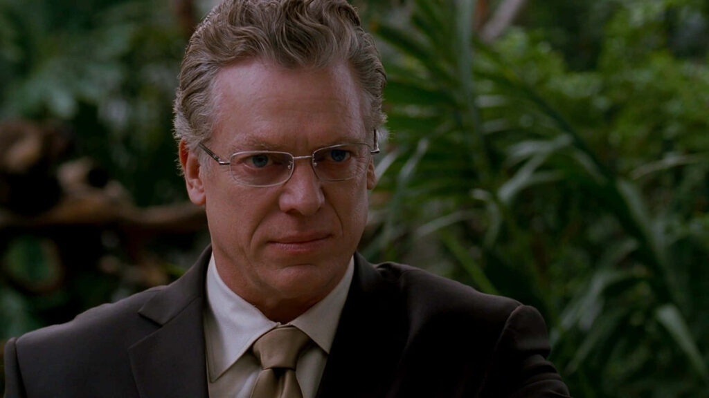 Christopher McDonald close-up in dark suit and glasses with lush green jungle background wallpaper