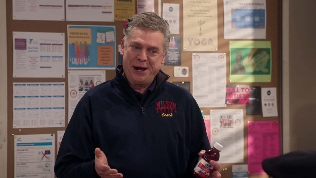 Christopher McDonald in Wilson Trinity Coach jacket holding bottle by colorful bulletin board indoors Wallpaper