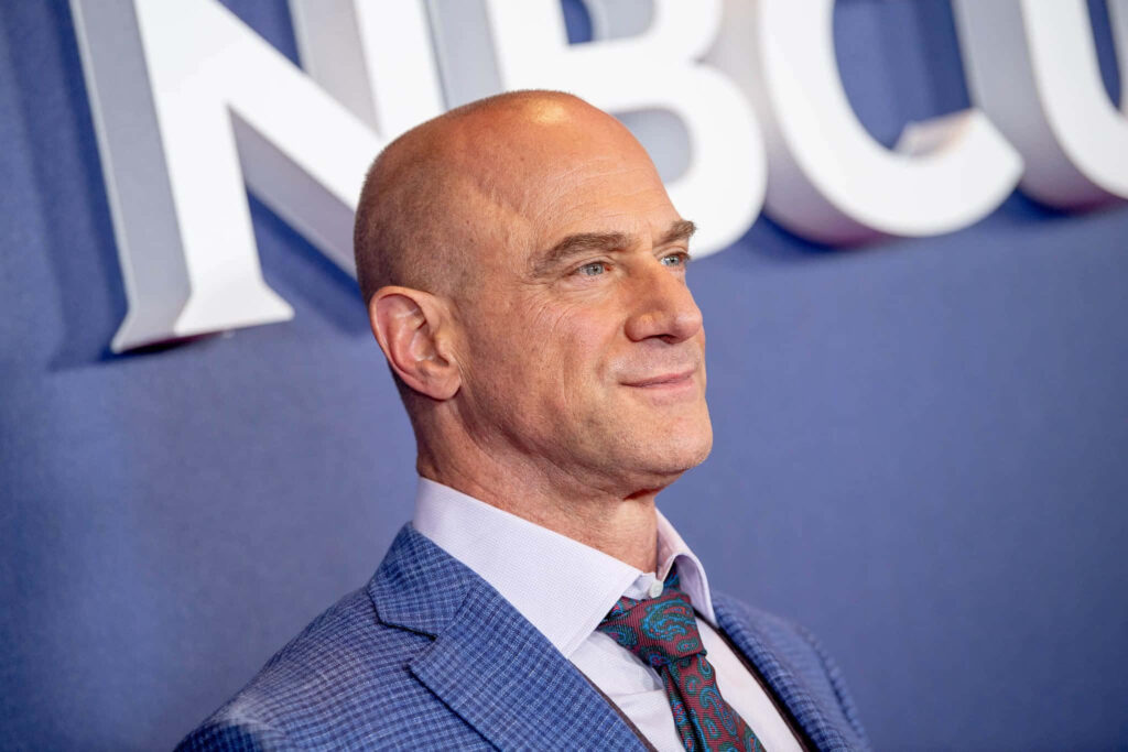 Christopher Meloni in blue checkered suit and patterned tie posing confidently at NBC backdrop Wallpaper