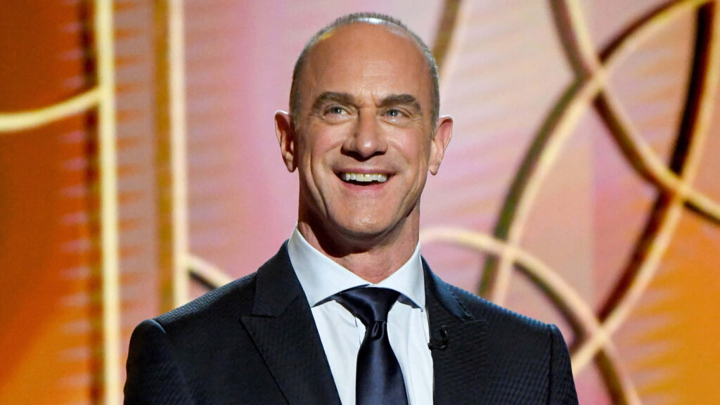 Christopher Meloni in formal suit smiling with golden abstract circular pattern wallpaper background