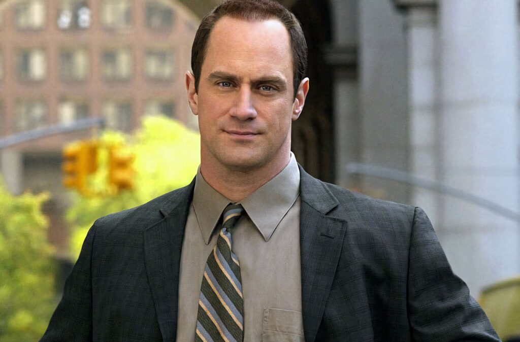 Christopher Meloni in sharp suit and striped tie against urban daylight backdrop professional look Wallpaper