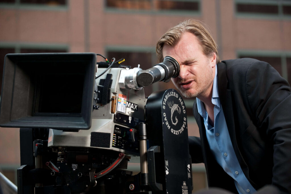 Christopher Nolan in classic suit filming with professional camera on urban set focused intense Wallpaper