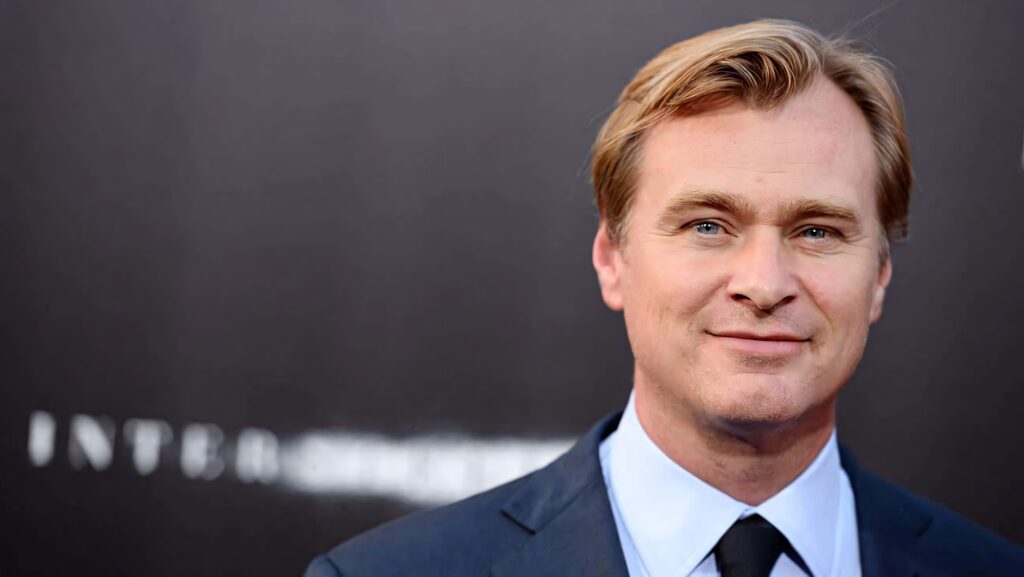 Christopher Nolan in navy suit and light blue shirt portrait with cinematic style and soft background Wallpaper