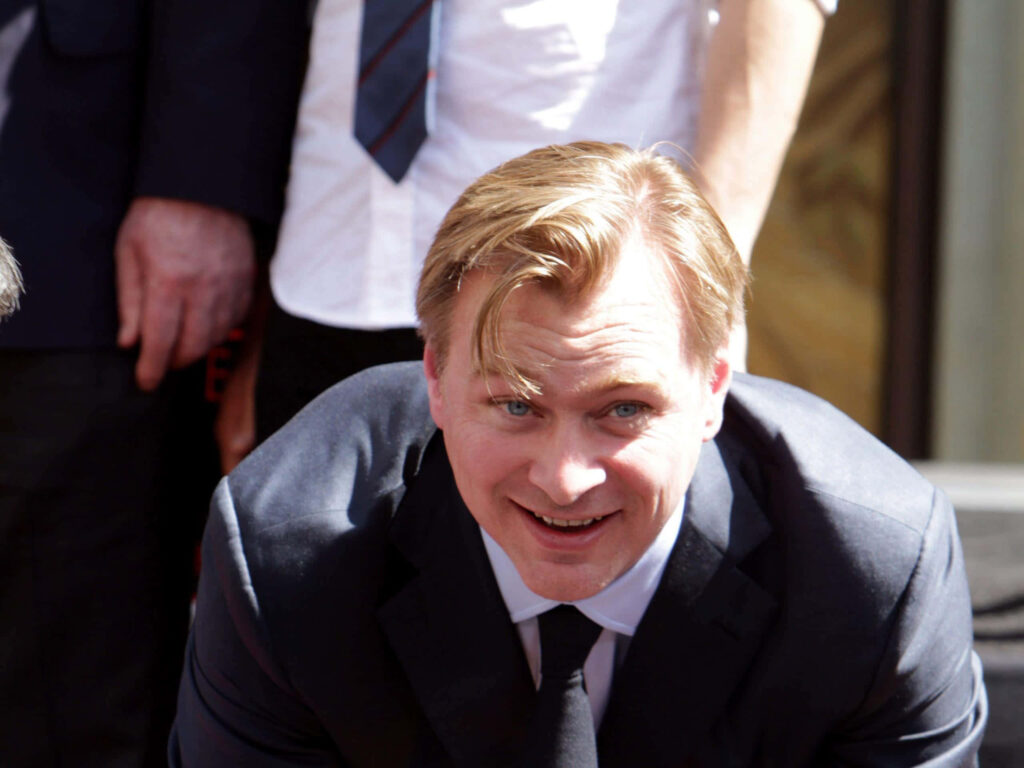 Christopher Nolan in black suit smiling candidly with blurred background film director wallpaper