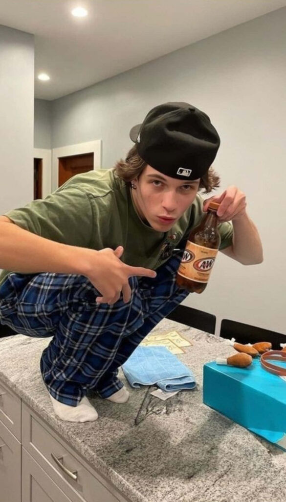 Christopher Sturniolo squatting on kitchen counter holding A&W root beer in casual attire Wallpaper