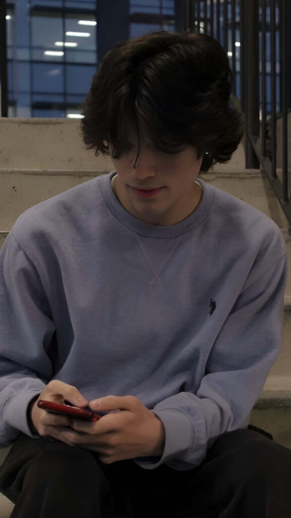Christopher Sturniolo seated on steps in light purple sweatshirt with modern architecture backdrop Wallpaper