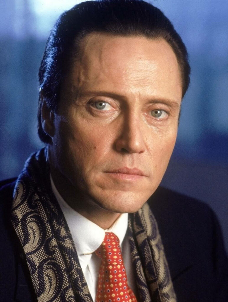 Christopher Walken headshot with intense blue eyes in suit and red tie against blurred background Wallpaper