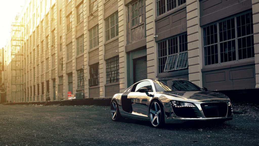 Chrome Audi R8 parked by industrial building in sunlight showcasing sleek modern design 4k wallpaper