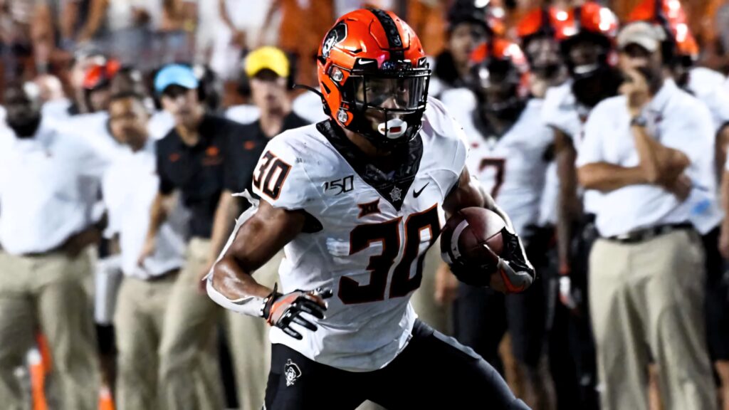 Chuba Hubbard in Oklahoma State uniform running with football during intense stadium game action Wallpaper