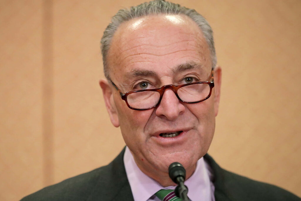Close-up portrait of Senator Chuck Schumer speaking with glasses and professional attire background Wallpaper