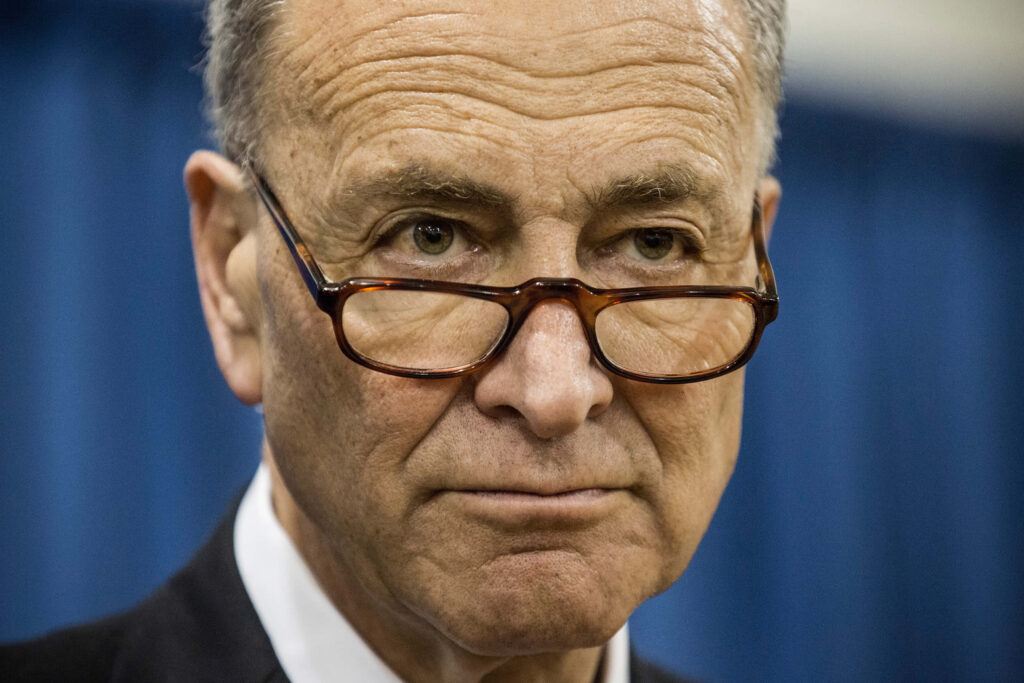Close-up portrait of Chuck Schumer with eyeglasses on blue blurred background wallpaper