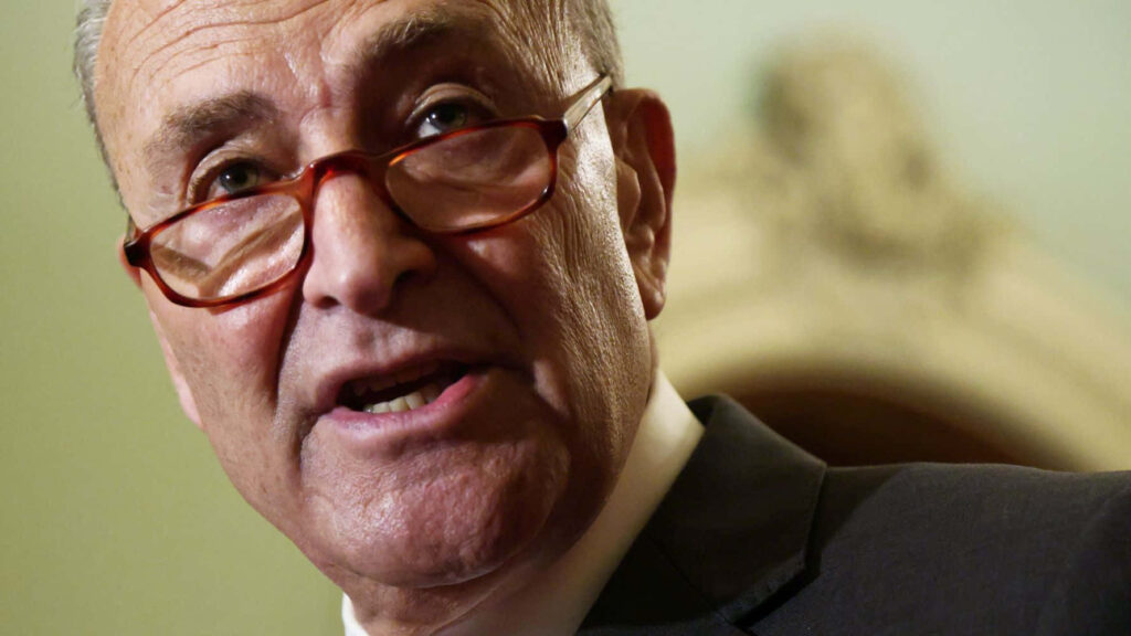 Close-up portrait of Chuck Schumer in red glasses with warm lighting and blurred background Wallpaper