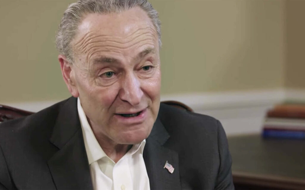 Close-up portrait of Chuck Schumer in dark suit with warm indoor lighting on neutral background Wallpaper