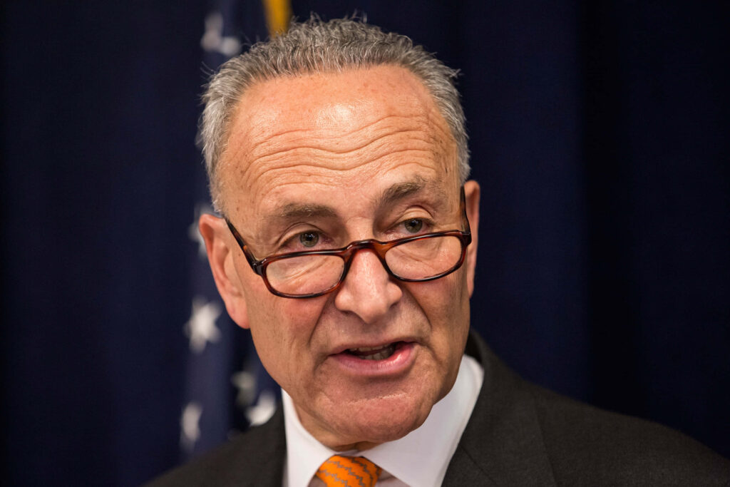 Chuck Schumer portrait wallpaper focused in suit and glasses with dark background and leadership theme