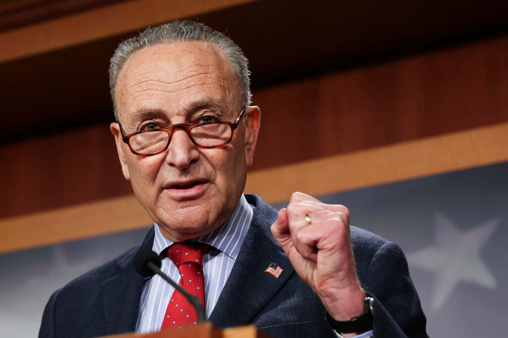 Chuck Schumer delivering speech with determined look warm lighting muted brown stars background wallpaper