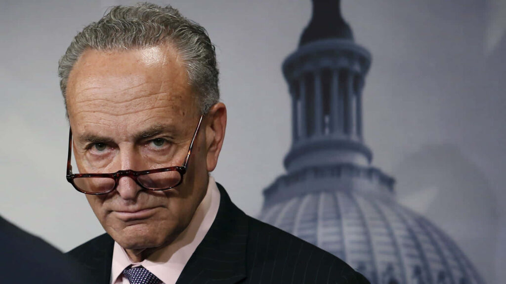 Chuck Schumer in dark suit and glasses with US Capitol dome backdrop serious political portrait Wallpaper