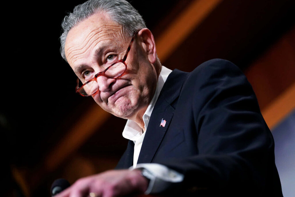 Chuck Schumer candid portrait in dark suit red glasses warm blurred background wallpaper