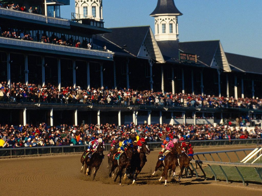 Jockeys racing thoroughbreds at Churchill Downs with twin spires and cheering crowd in daylight Wallpaper