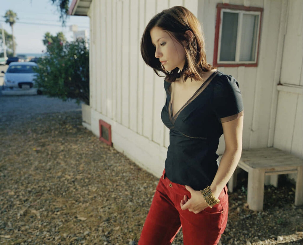Chyler Leigh in black top and red pants outside rustic white house calm thoughtful mood wallpaper