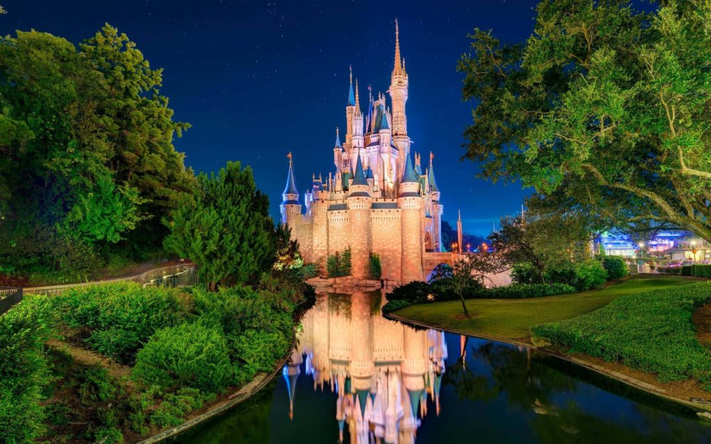Cinderella Castle glowing at night with starry sky and reflection in Magic Kingdom moat wallpaper