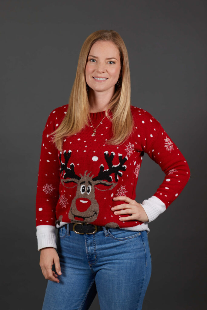 Cindy Busby in festive red reindeer sweater smiling against dark holiday wallpaper background