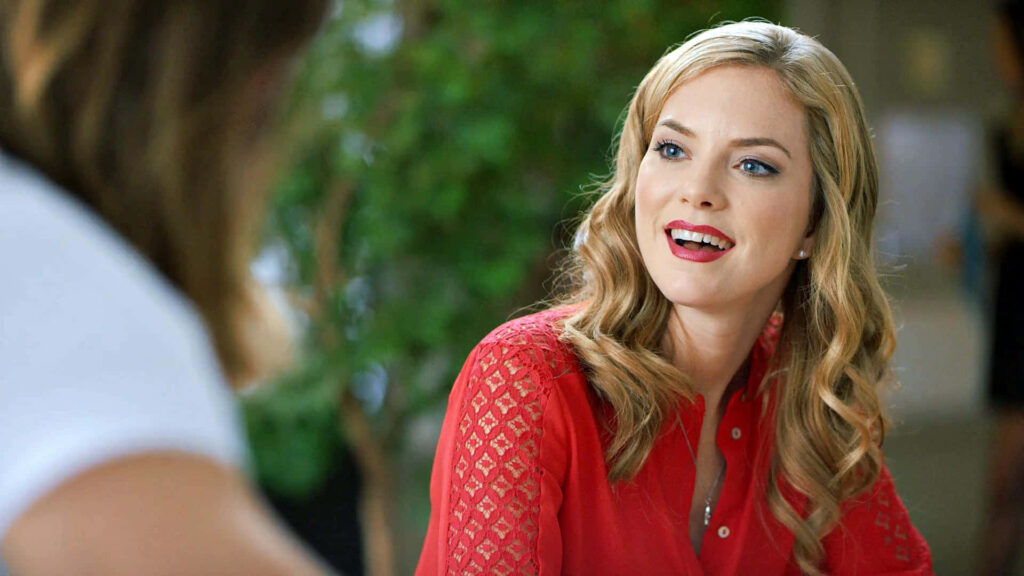 Cindy Busby smiling in red blouse with soft blonde waves green blurred background wallpaper