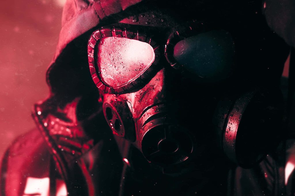 Close-up of a hooded figure in gas mask with red lighting and moisture droplets post-apocalyptic wallpaper