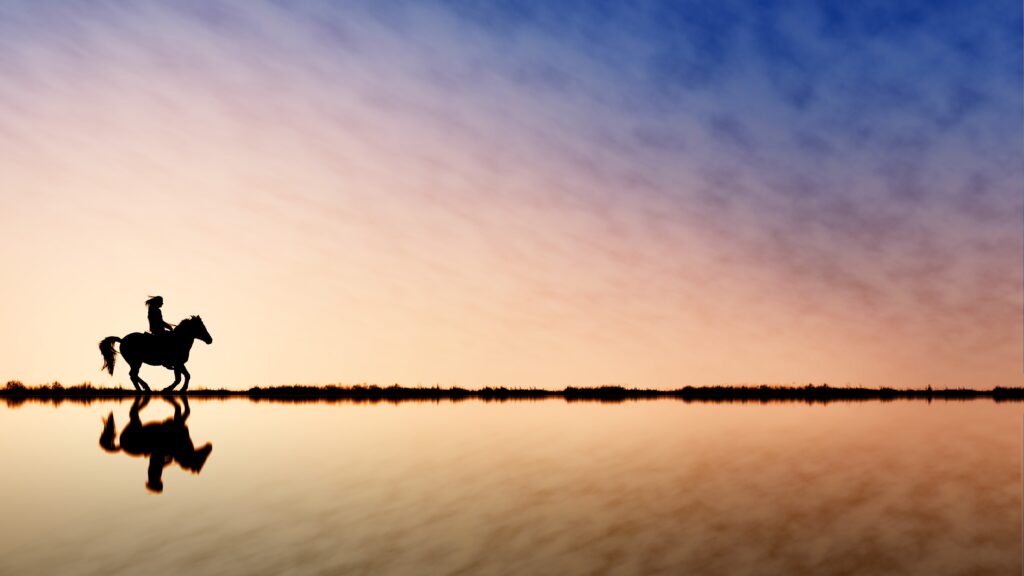 Silhouette of horseback rider at sunset with blue peach sky and calm water reflection wallpaper