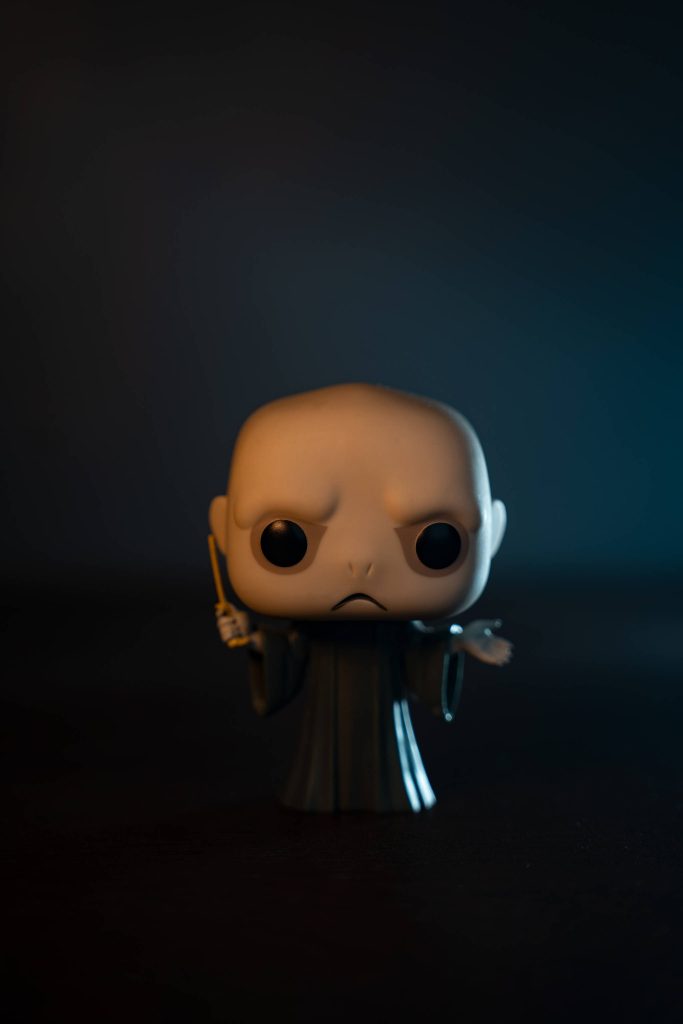 Close-up cinematic Lord Voldemort Funko Pop holding wand with warm glow and moody blue background Wallpaper