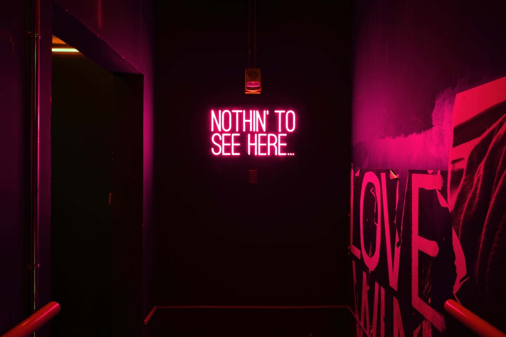 Glowing neon NOTHIN TO SEE HERE sign in dark corridor with red and magenta lights wallpaper