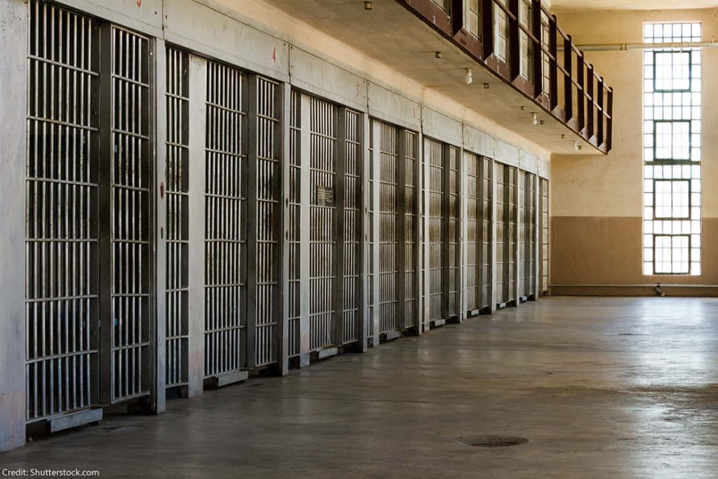 Cinematic prison corridor with metal-barred jail cells and natural light for gritty wallpaper background
