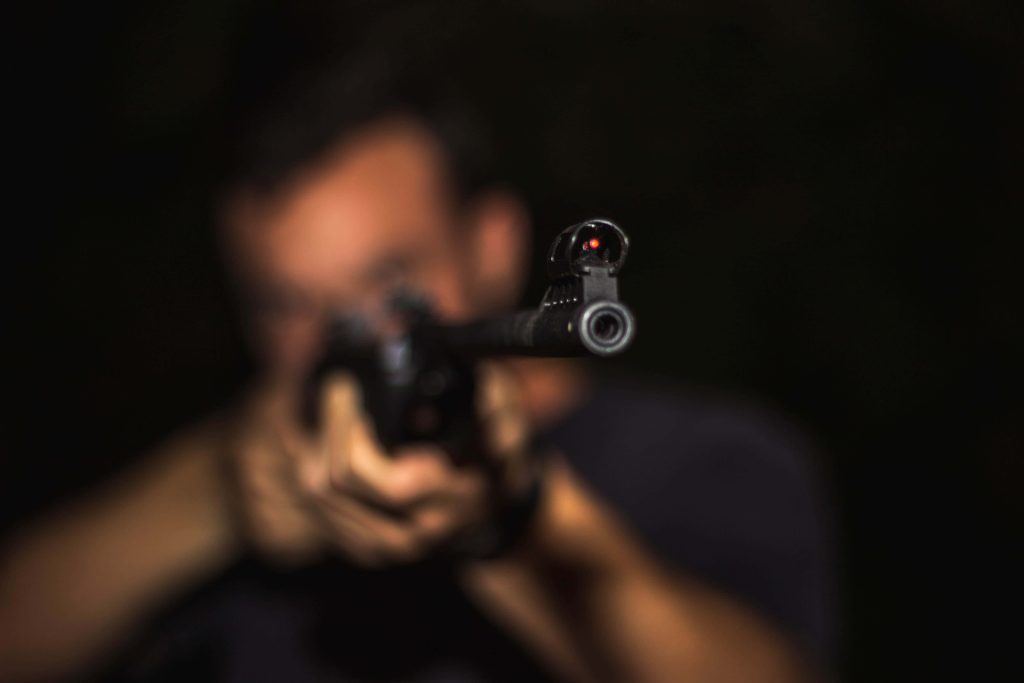 Close-up of rifle with glowing red fiber optic sight against dark blurred background cinematic gun Wallpaper