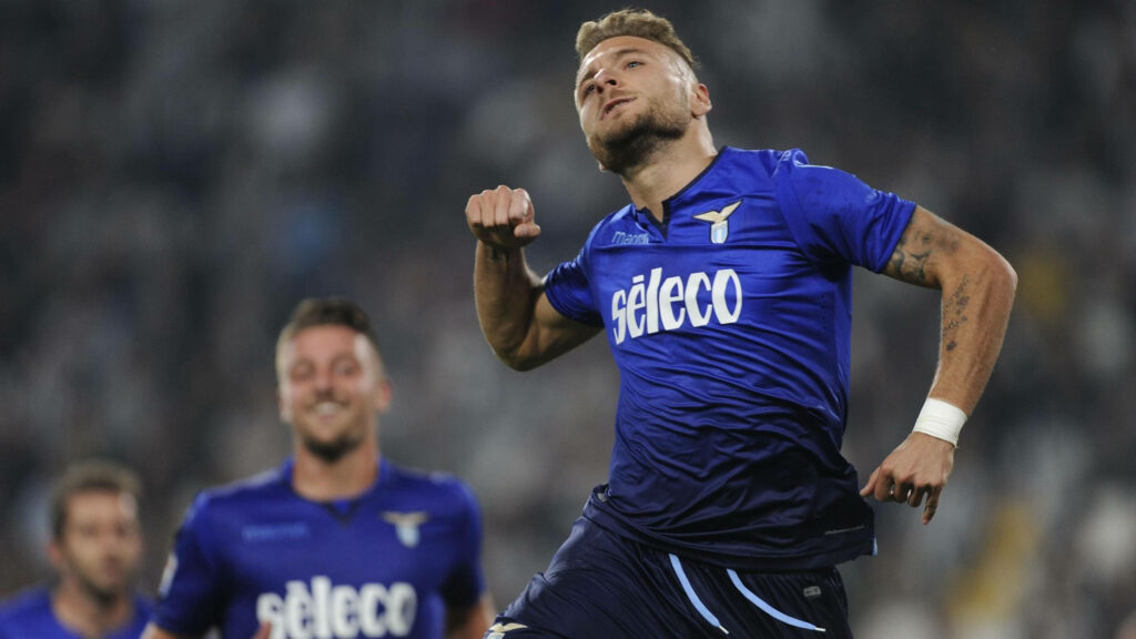 Ciro Immobile celebrating in Lazio blue kit with Seleco logo in dynamic stadium action shot Wallpaper