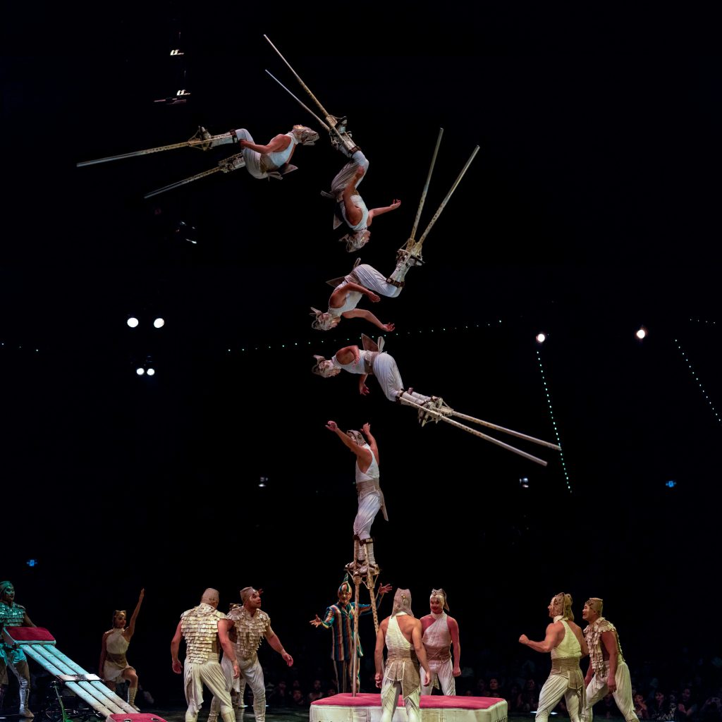 Acrobat on stilts leaping in dramatic Cirque du Soleil performance with textured costumes Wallpaper