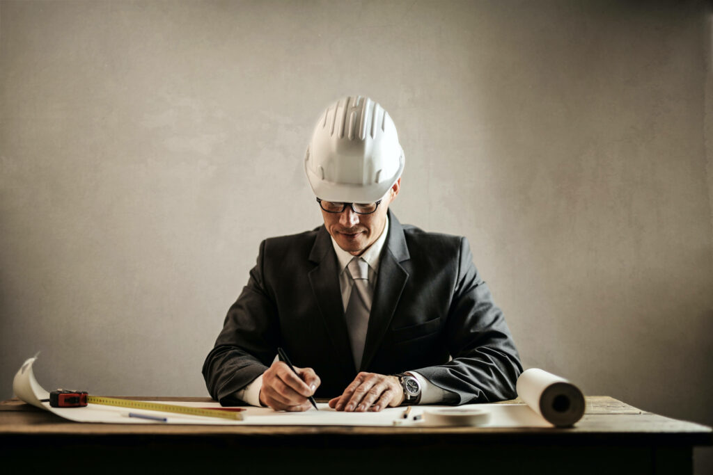 Civil engineer in suit with white helmet drafting detailed construction blueprints at desk Wallpaper