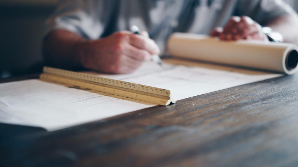 Close-up of civil engineer drafting technical plans with blueprint and ruler on wooden desk Wallpaper
