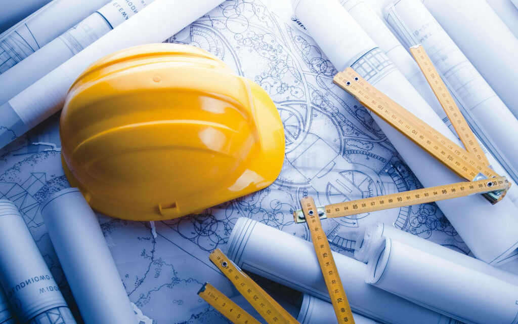 Yellow hard hat on blueprints with measuring tools and architectural plans construction background Wallpaper
