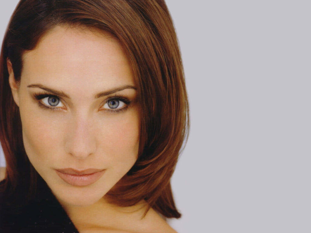 Close-up portrait of Claire Forlani with blue eyes soft brown hair on minimalist gray wallpaper background