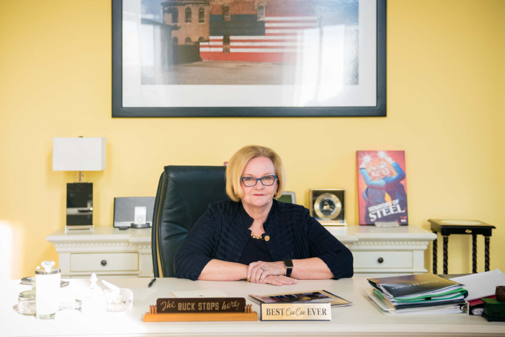 Claire McCaskill at Senate desk in bright office with American flag art and yellow walls background Wallpaper