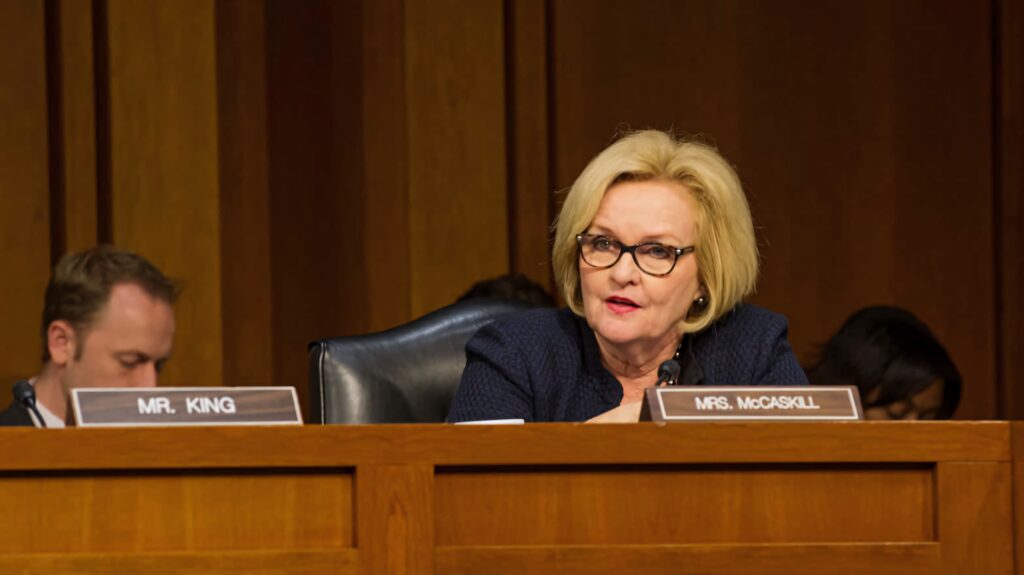 Claire McCaskill speaking passionately at hearing seated at wooden desk with nameplate and warm lighting Wallpaper