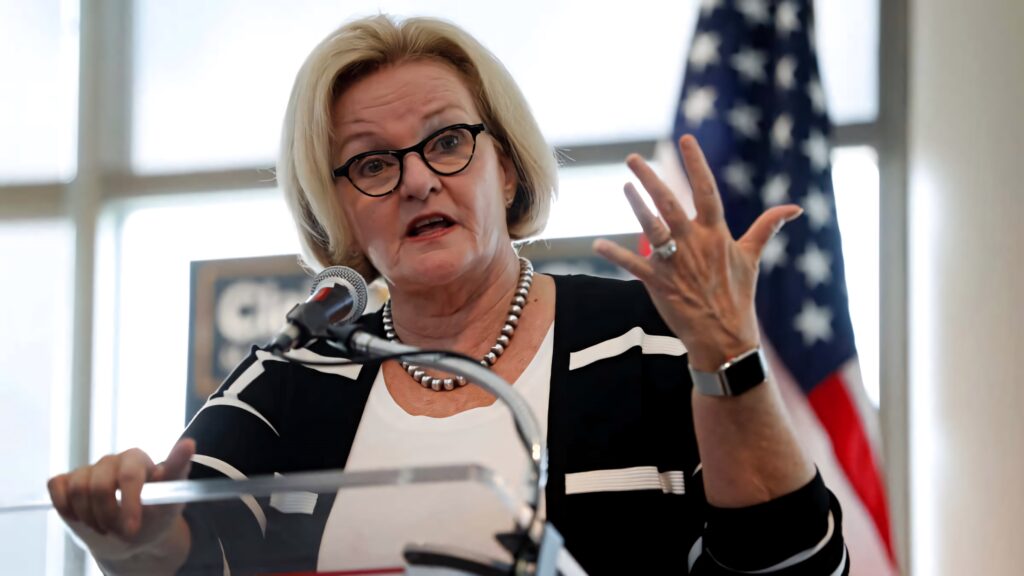 Claire McCaskill speaking at podium with US flag backdrop in bright professional setting wallpaper