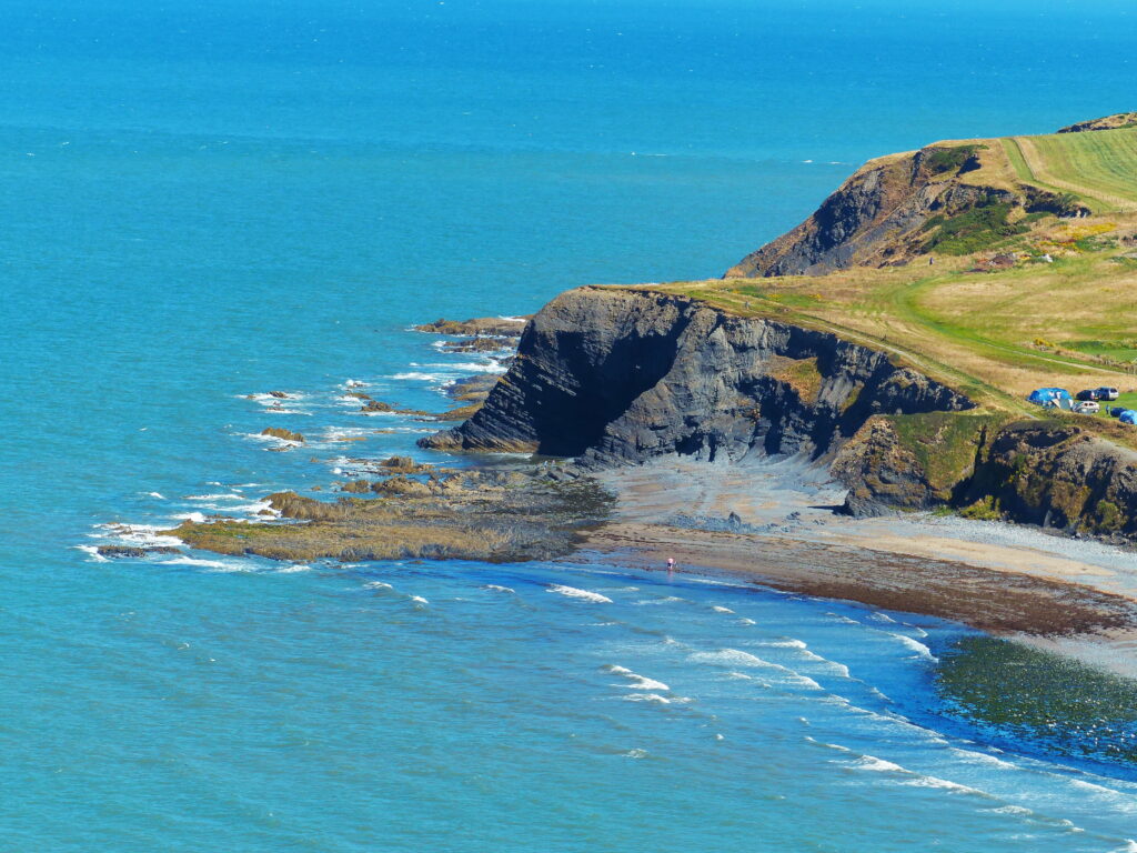 Clarach Bay Wales cliffs and green hills meet turquoise sea with gentle waves under blue sky wallpaper