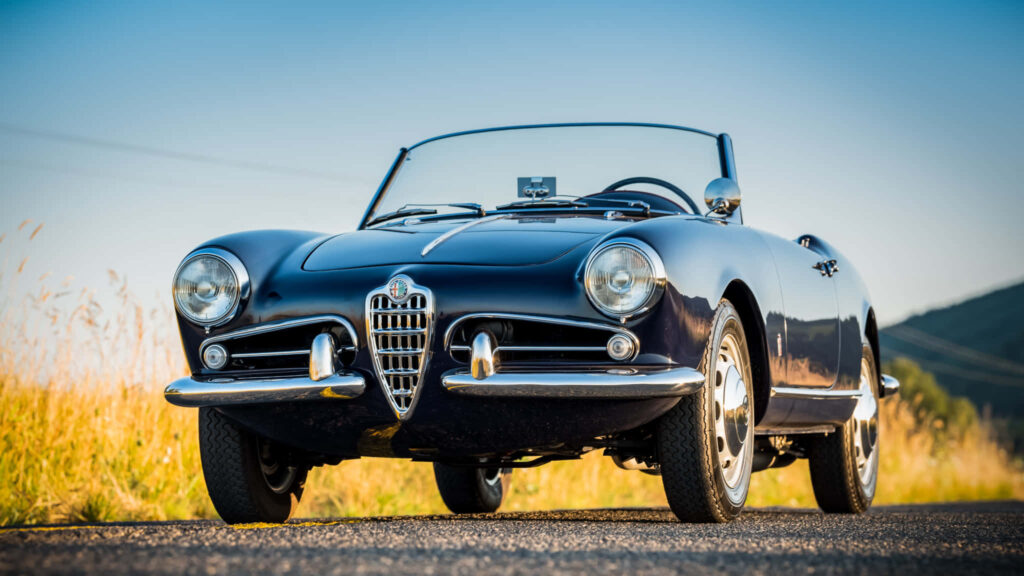 Classic Alfa Romeo Spider convertible driving on open road under clear blue sky wallpaper background