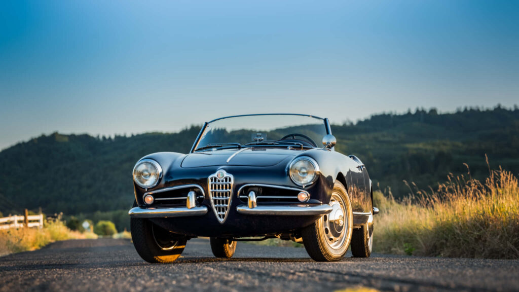 Classic Alfa Romeo Spider convertible parked on rural road with rolling hills and clear sky wallpaper