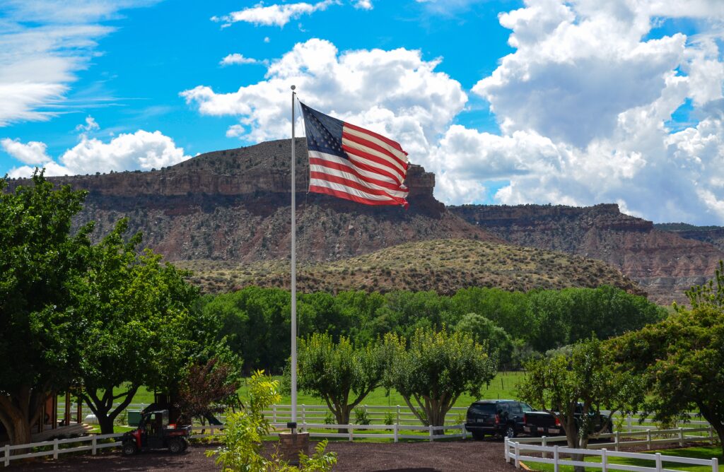 American ranch scene Utah with US flag red rock cliffs green fields and rural farm elements wallpaper